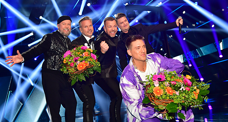 De fyra killarna i Arvingarna står med blommor och är glada. Framför dem sitter Danny Saucedo på huk med blommor. Han är också glad.