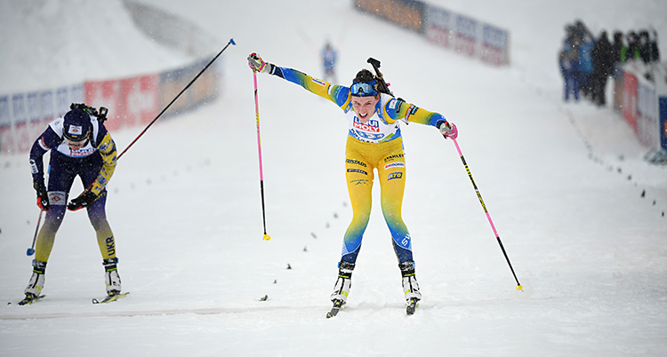 Från ett lopp i skidskytte. Det är upplopp och två åkare kämpar om att komma först. Hanna Öberg från Sverige har en gul dräkt.