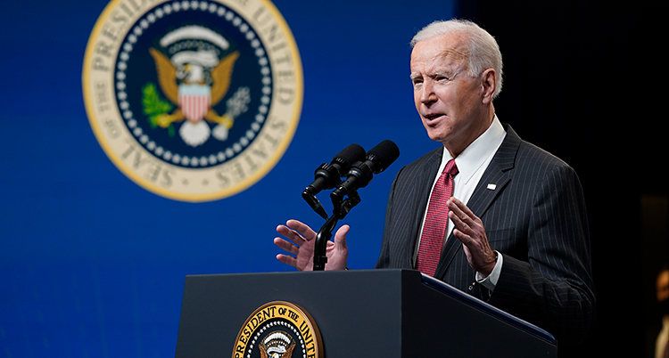 Joe Biden står och pratar i en talarstol. Han har vitt hår. Han har kostym och slips.