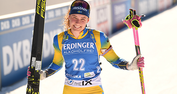 Hanna Öberg ler och tittar in i kameran. Hon håller i sina skidor och sina stavar.