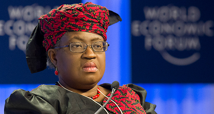 Ngozi Okonjo-Iweala sitter på ett möte. Hon har glasögon. Hon har en dräkt som är röd och svart. Hon har en röd duk snurrad runt huvudet.