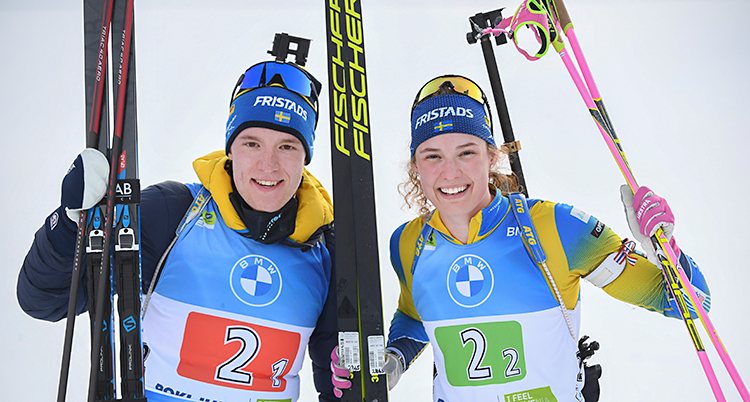 Sebastian och Hanna är glada. De tittar in i kameran. De håller i sina skidor och stavar.