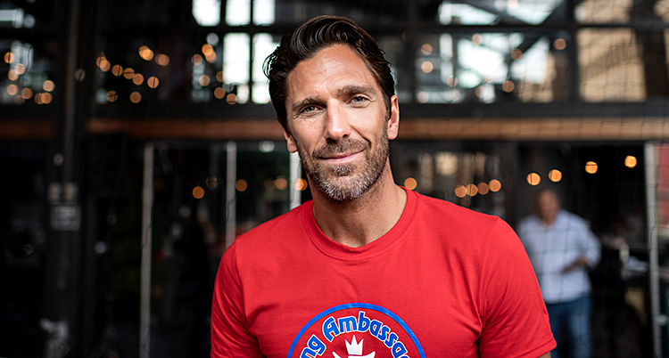 Henrik Lundqvist tittar in i kameran. Han ler. Han har brunt hår. Han har en röd tröja.