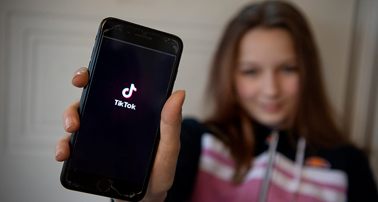 Hon håller i en mobiltelefon där startsidan på Tiktok syns,