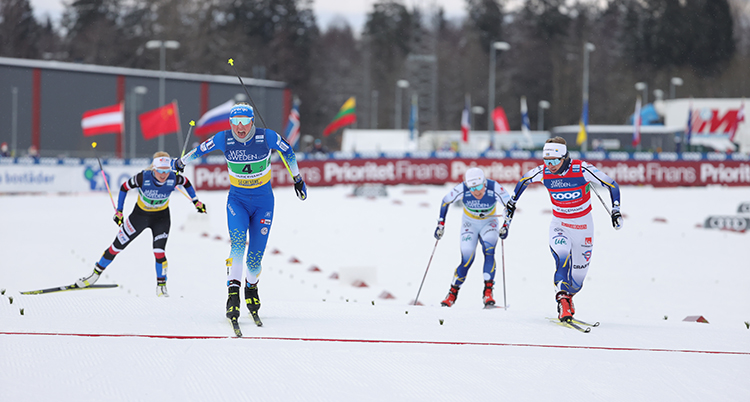 Fyra skidåkare kör mot mållinjen på en snöig skidarena