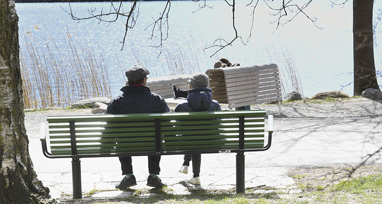 Två personer sitter på en bänk. Solen skiner.