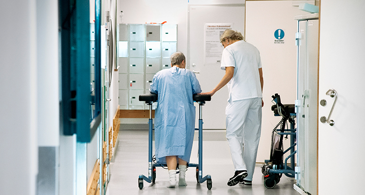 En kvinna går med rollator i en korridor.
