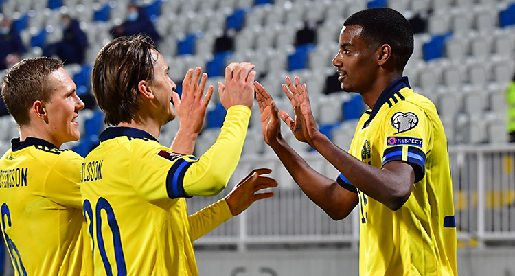 Bilden är från en match i fotboll. Tre spelare från Sverige firar ett mål. De har gula tröjor.
