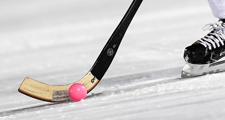 Bilden är tagen på en plan av is. Någon spelar bandy. Det är en närbild på en klubba, en boll och en skridsko.