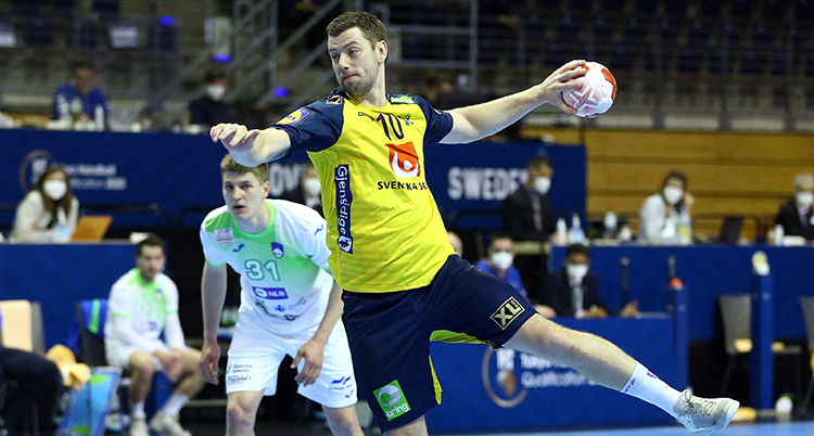 Han hoppar upp i luften med högre arm framsträckt. Vänster arm är bakom kroppen och håller i handbollen, redo att skjuta den.