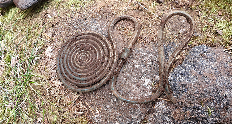 Ett spänne av brons. Det är en platt spiral och en slags krok går ut från den.