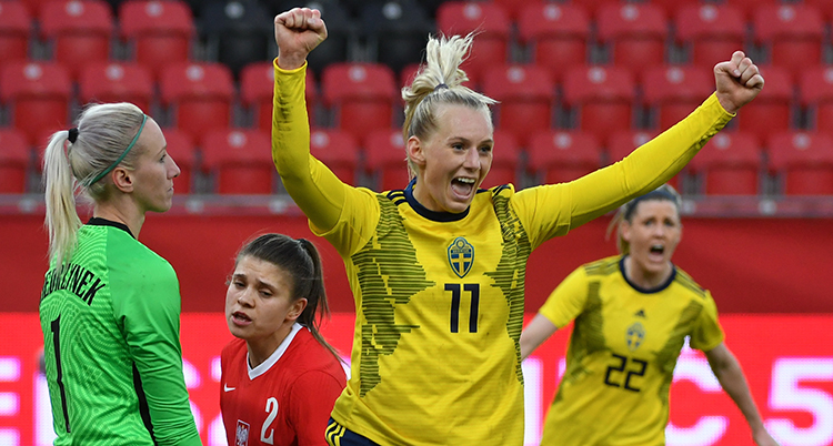 Stina Blackstenius sträcker armarna i luften och ser glad ut. Bredvid henne står Polens målvakt och ser uppgiven ut.