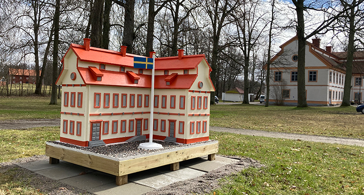 Ett litet hus som ser ut som en kopia av den större beiga herrgården står på en gräsmatta