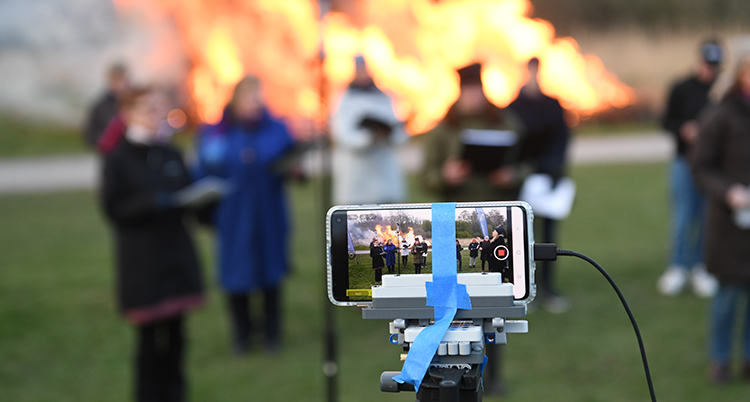 En mobilkamera som filmar några som sjunger framför en stor eld.