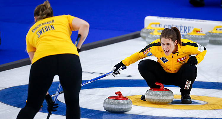Från en match i curling. Knochenhauer följer med stenen. Hasselborg sitter inne i boet och skriker. De har gula tröjor på sig.