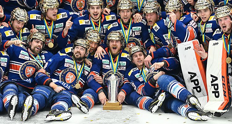 Hela Växjös lag är samlat på isen. De är glada och firar. De har guldhjälmar på sig. Pokalen står i mitten, på isen.