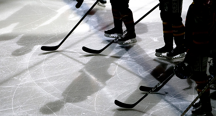 Ishockeyspelare med klubbor på isen. Bara deras skridskor och klubbor syns.