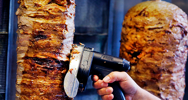 Närbild på en rulle kött någon skär bitar av.