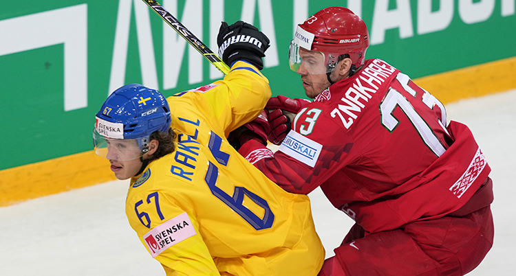 En spelare i gul tröja blir attackerad av en spelare i röd tröja. De är på isen nära rinken.