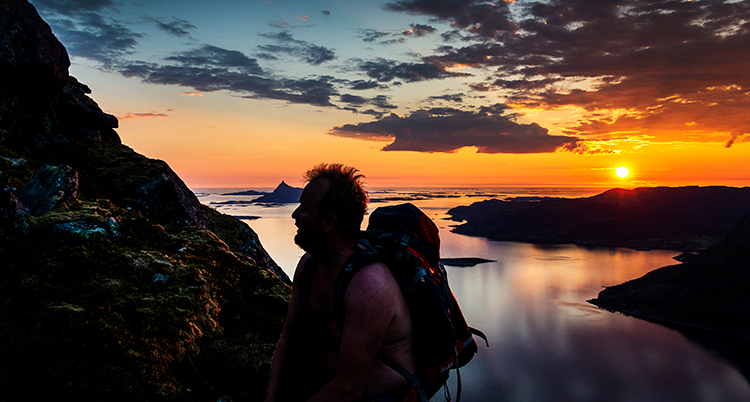 En vacker solnedgång i bakgrunden. En man klättrar på ett berg i förgrunden, vi ser bara siluhetten.