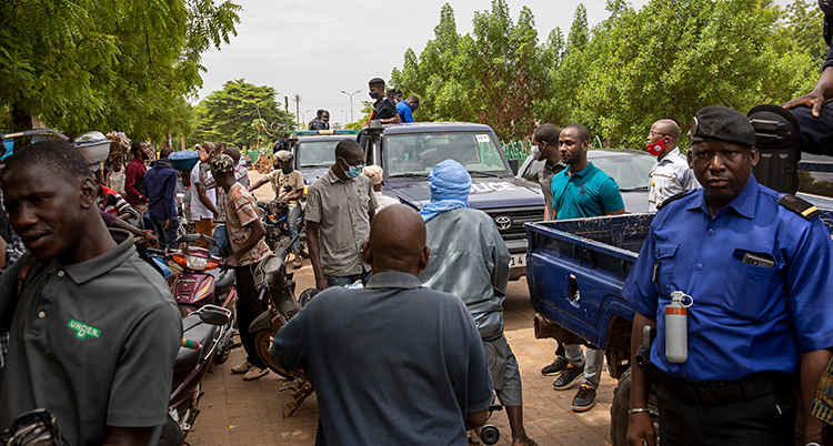 Bilden är från en gata i staden Bamako i Mali. Det är fullt av bilar och människor på gatan. Bredvid gatan växer buskar och träd.