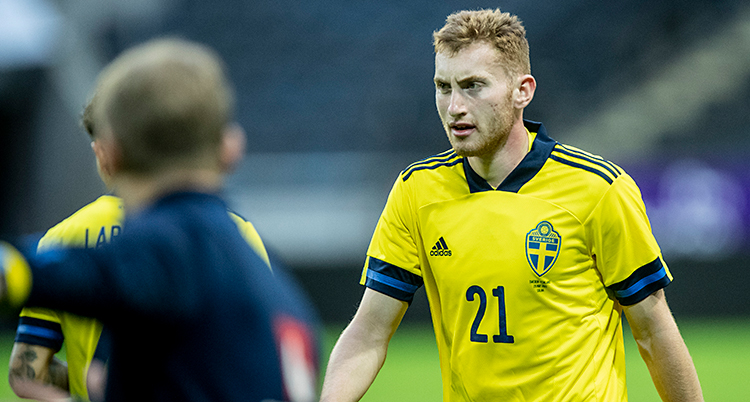 Bilden är tagen på en fotbollsplan. Dejan Kulusevski går på planen. Han har på sig Sveriges gula tröja.