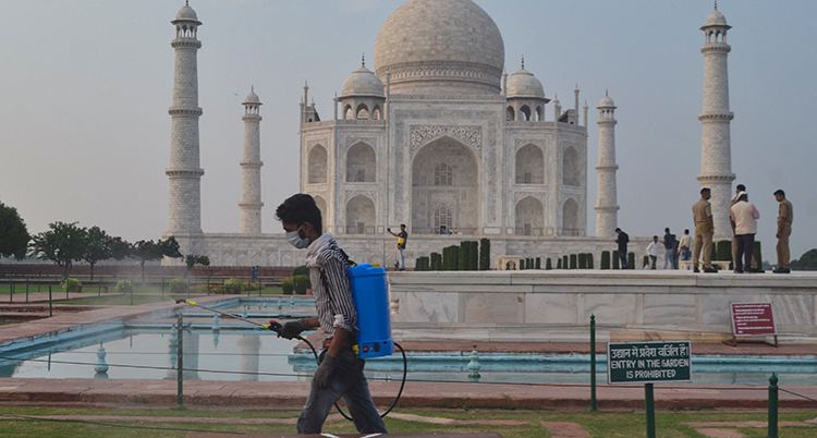En man med munskydd och maskin på ryggen sprutar och rengör framför byggnaden Taj Mahal.