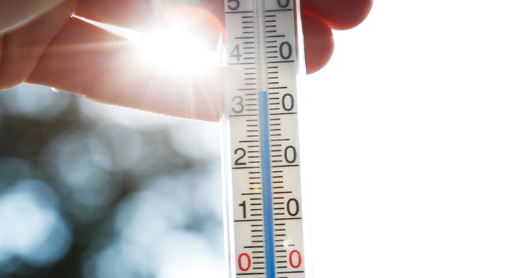 En hand håller en termometer som visar på över 30 grader.