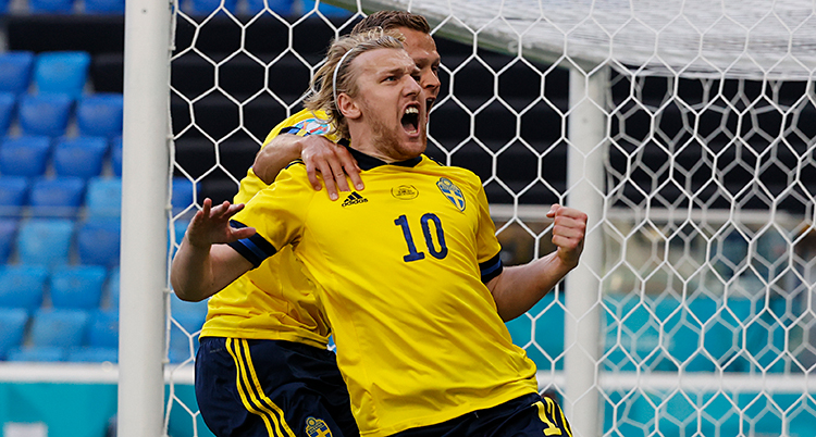 Från en match i fotboll. Emil Forsberg har gjort mål på straff. Han skriker och jublar. Han blir kramad bakifrån av en annan svensk spelare.