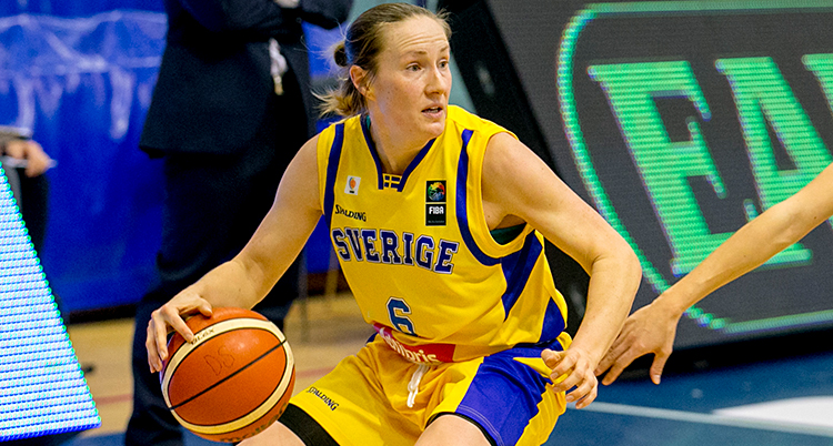 Från en match i basket. Frida Eldebrink har bollen. Hon har gula kläder med blå detaljer. Det står Sverige i blått på bröstet.
