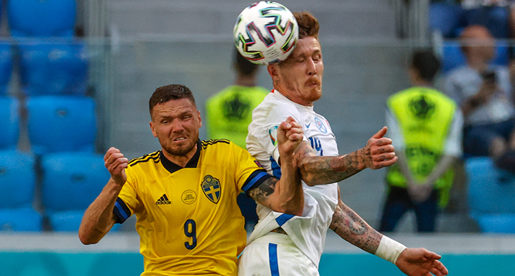 Två spelare hoppar. De försöker nicka. Slovaken har träffat. Båda blundar och grinar illa.