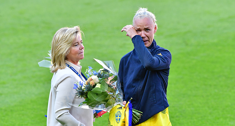 Caroline Seger torkar bort en tår. En kvinna står framför henne och ger henne blommor.