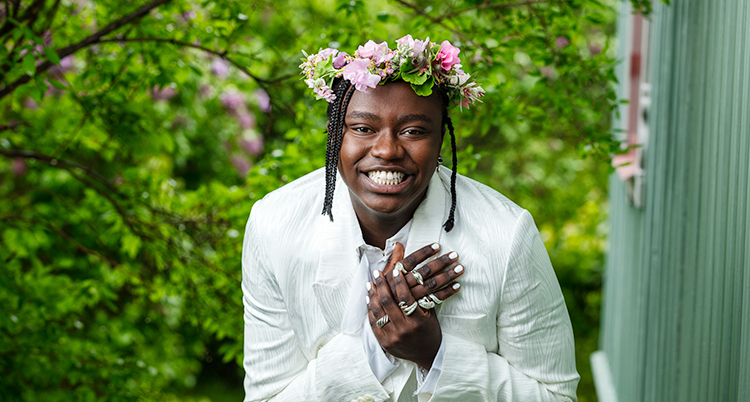 Han har en krans med blommor i håret. Han ler.