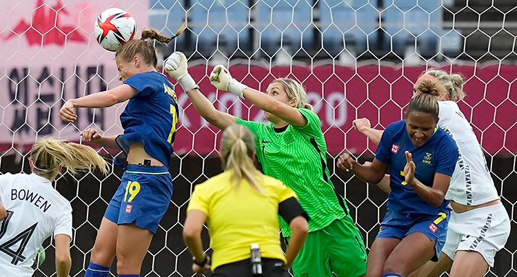 Från en match i fotboll. Många personer är framför målet. En person nickar bollen.