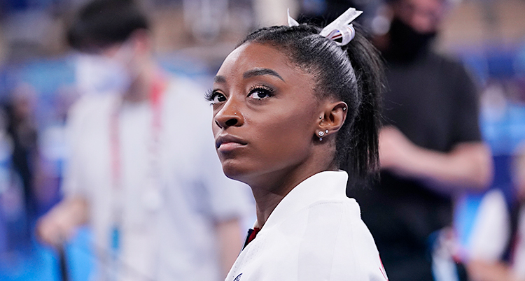 En närbild på Simone Biles. Hon tittar snett uppåt i bilden. Hon har håret uppsatt i en tofs.