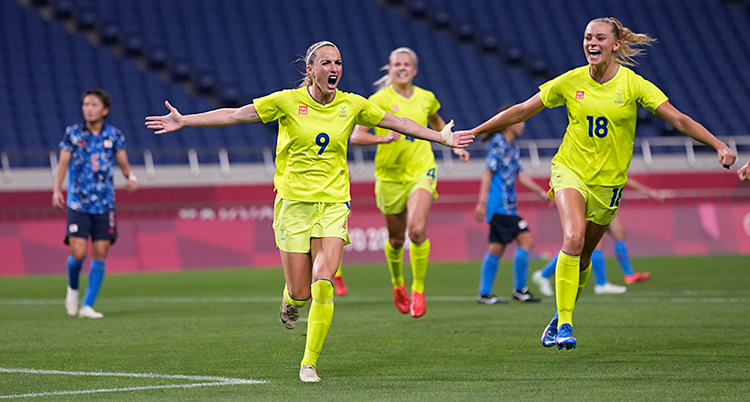 Från en match i fotboll. Kosovare Asllani springer och ropar av glädje. Flera spelare springer fram mot henne. Alla har gula kläder.