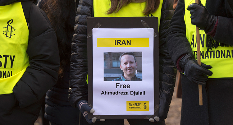 MÄnniskor i gula västar som det står Amnesty på, håller ett plakat framför sig med bild på Djalali och en krav på att han blir fri.