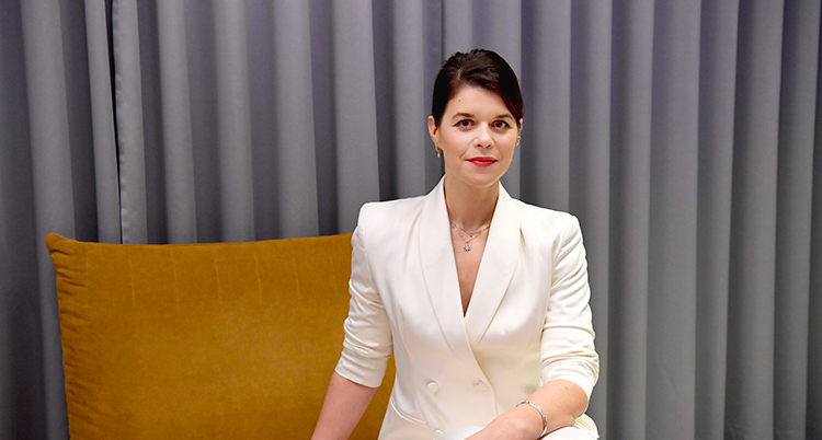 Emma molin klädd i vit kostym sitter i en brandgul fåtölj.