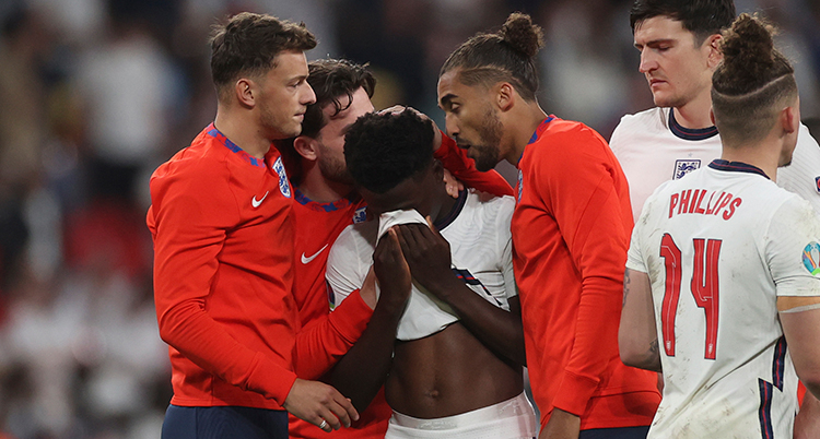 Englands spelare Bukayo Saka tröstas av sina lagkamrater efter att han missat sin straff.