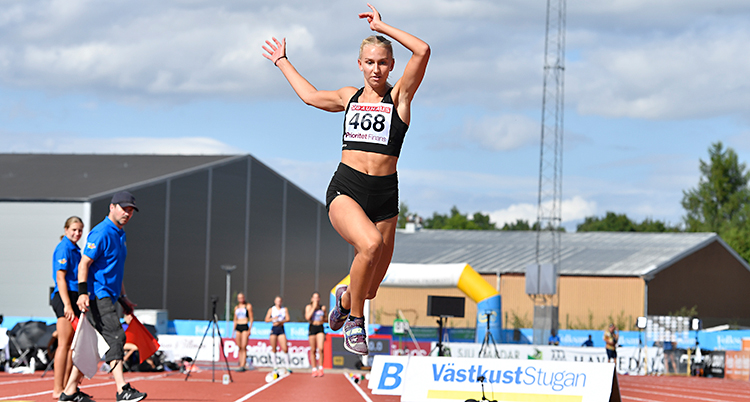 Maja Åskag är mitt i ett hopp. Hon är i luften. Hon tävlar i en svart dräkt.