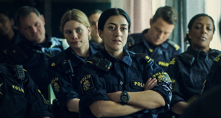 Poliser sitter i ett rum, kvinnan närmast kameran har armarna i kors.