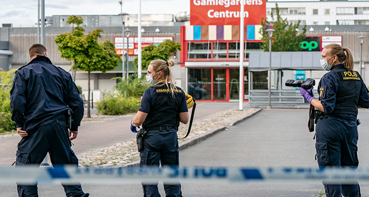 Tre poliser står med ryggen mot kameran. Bakom dem är ingången till köpcentret.