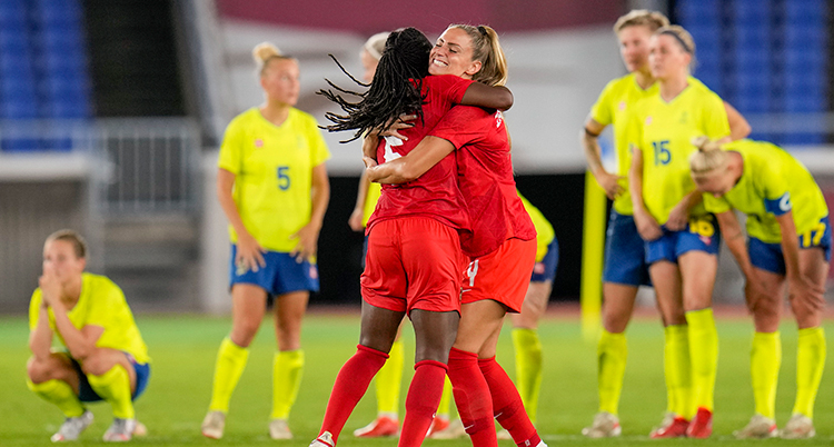Två fotbollsspelare i röda kläder kramar varandra, besvikna spelare i gult syns bakom.