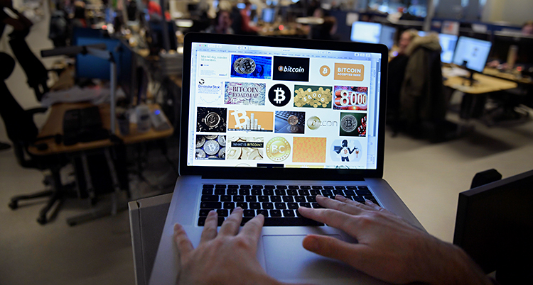 En person sitter vid en dator. Vi ser bara personens händer. På datorn finns det bilder där det står bitcoin.