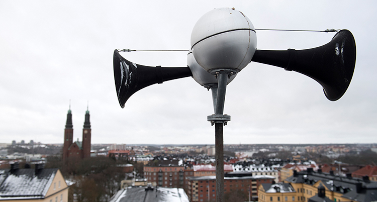 Ett larm sitter på en stålpinne. Bakom syns en stad.