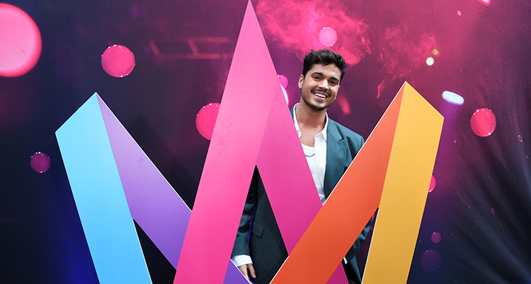 Han ler bakom den färgglada loggan för Melodifestivalen.