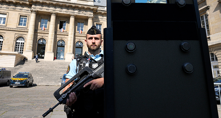 En polis står med ett stort vapen och vaktar framför domstolsbyggnaden.