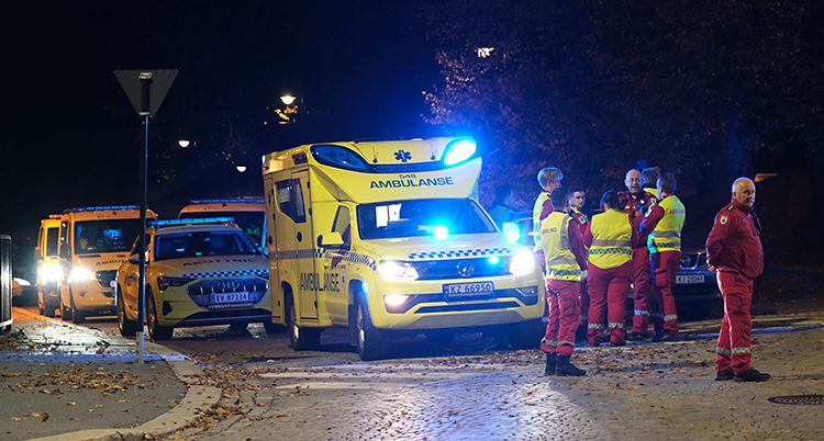 Bilden är tagen utomhus. Det är mörkt. Flera ambulanser står på rad. Personal står utanför.