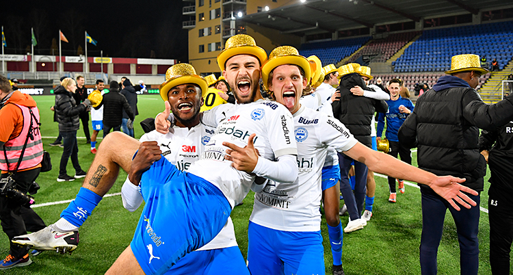 Efter en match i fotboll. Tre spelare är glada och tittar in i kameran. De har guldhattar.