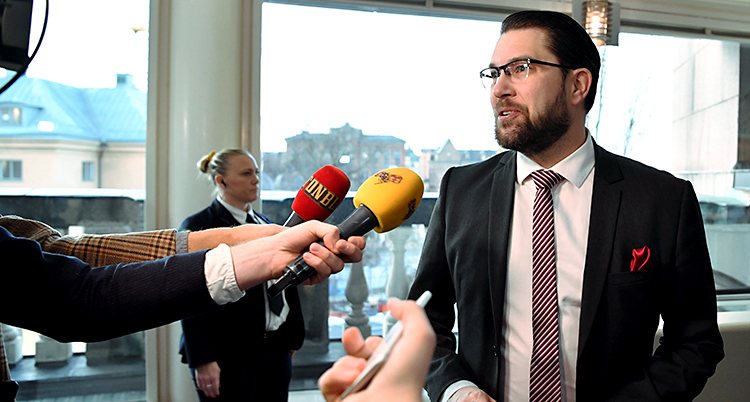 Jimmie Åkesson pratar med journalister och ser glad ut. Han har en mörk kostym.